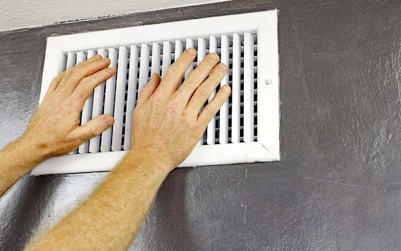 two hands in front of air vent on black wall