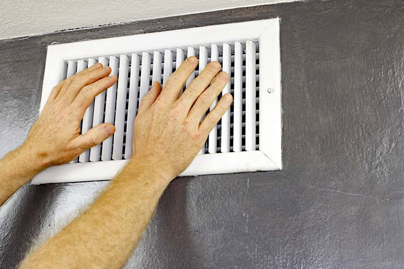 two hands in front of air vent on black wall