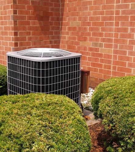 Outside residential heat pump unit by a red brick building. Transitioning your heat pump.