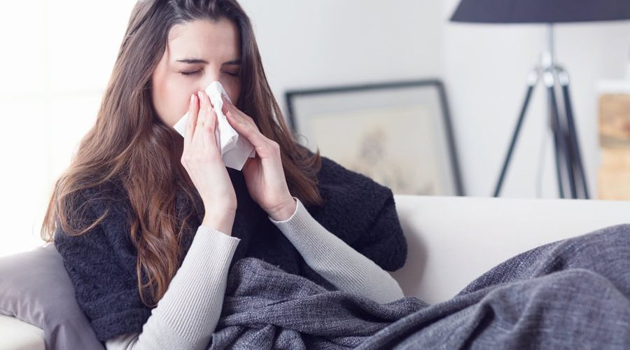 Young attractive woman lying sick at home couch in cold and flu sneezing nose with tissue covering with blanket. What Does Indoor Air Quality Have to Do With Allergies?
