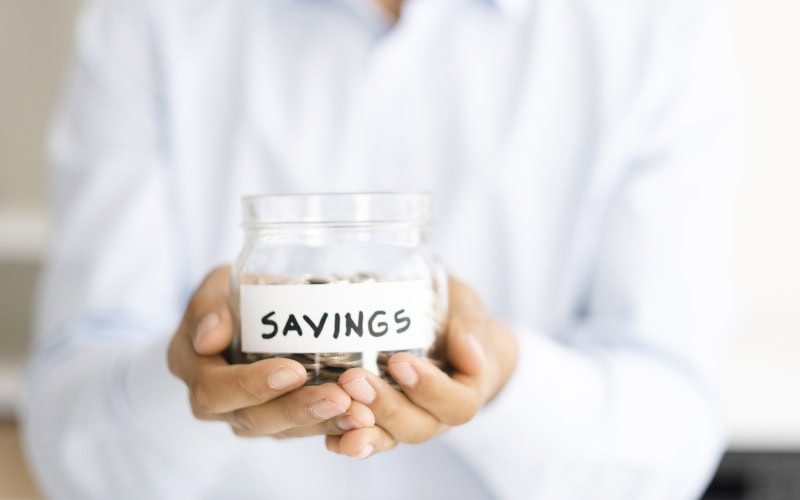 Why Buying a Heat Pump Instead of a Furnace Makes Sense. Photo of a person holding a jar of coins labeled "Savings".