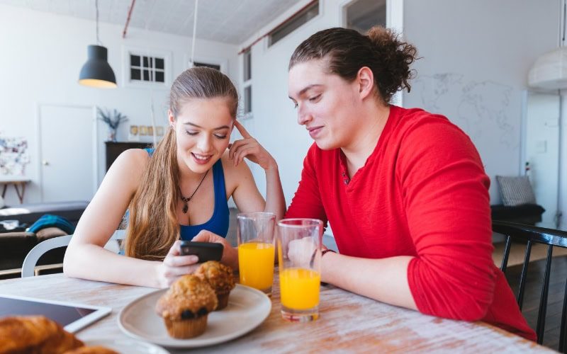 Young couple using phone to check social media feed over breakfast.