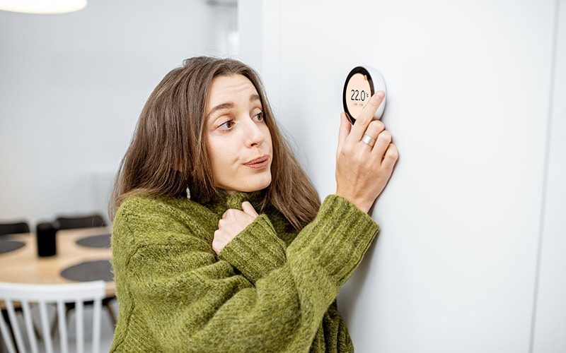Why Is My Heat Pump Turning On and Off Frequently? A lady turning up her thermostat.