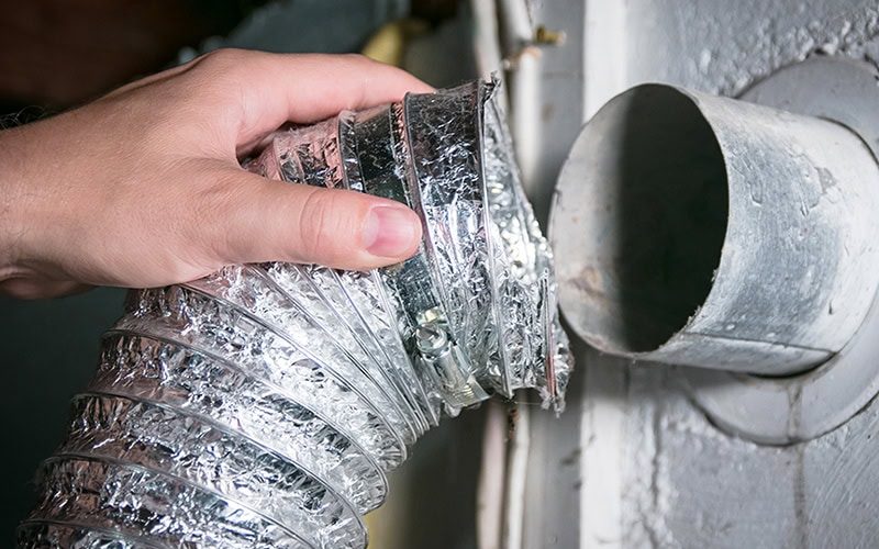 Duct Cleaning. Close up photo of a person pulling apart a dryer vent to clean.