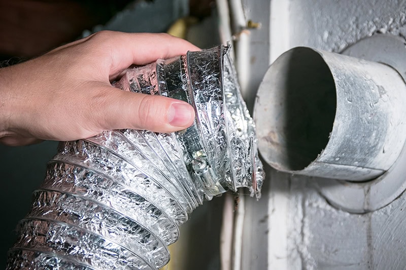 Duct Cleaning. Close up photo of a person pulling apart a dryer vent to clean.