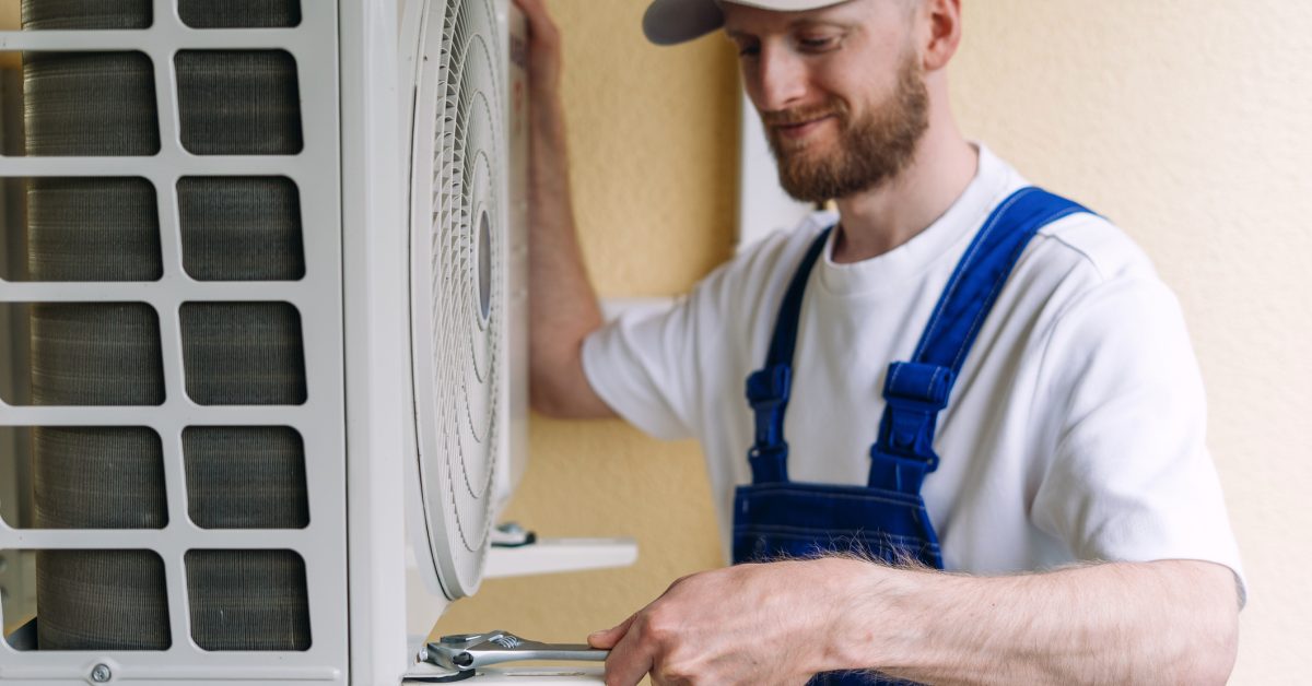 An HVAC technician in blue overalls and a cap uses a wrench during an AC replacement in Picayune.