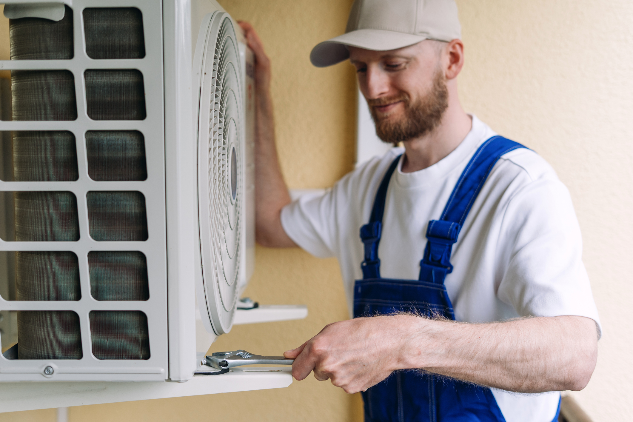 An HVAC technician in blue overalls and a cap uses a wrench during an AC replacement in Picayune.