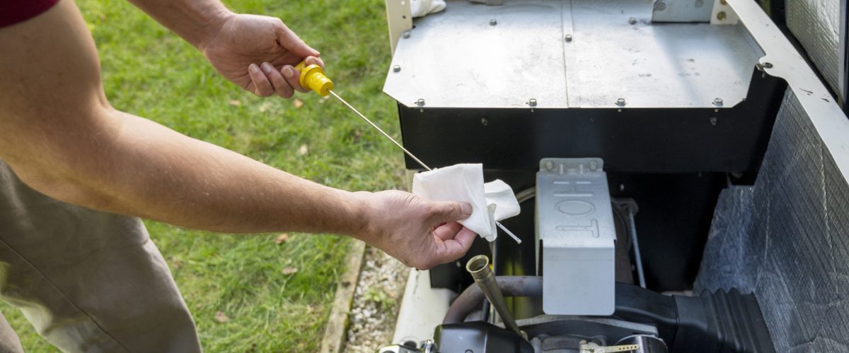 Man checking oil level on a home generator engine with a dipstick, wiping it clean with a paper towel outdoors.