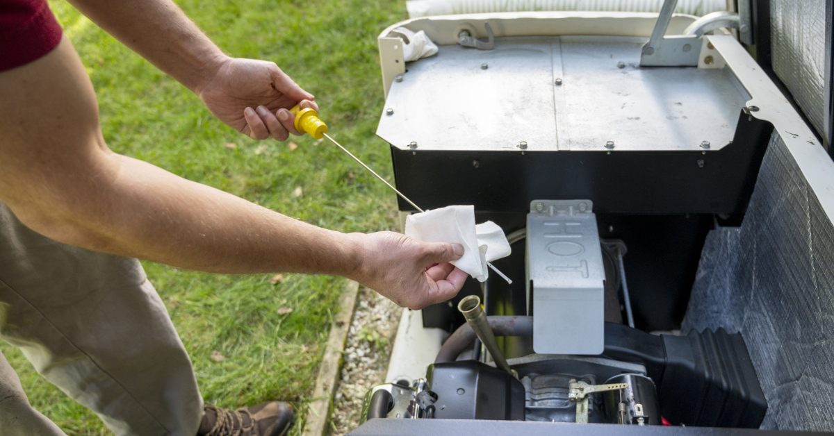 Man checking oil level on a home generator engine with a dipstick, wiping it clean with a paper towel outdoors.