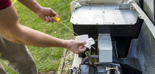Man checking oil level on a home generator engine with a dipstick, wiping it clean with a paper towel outdoors.