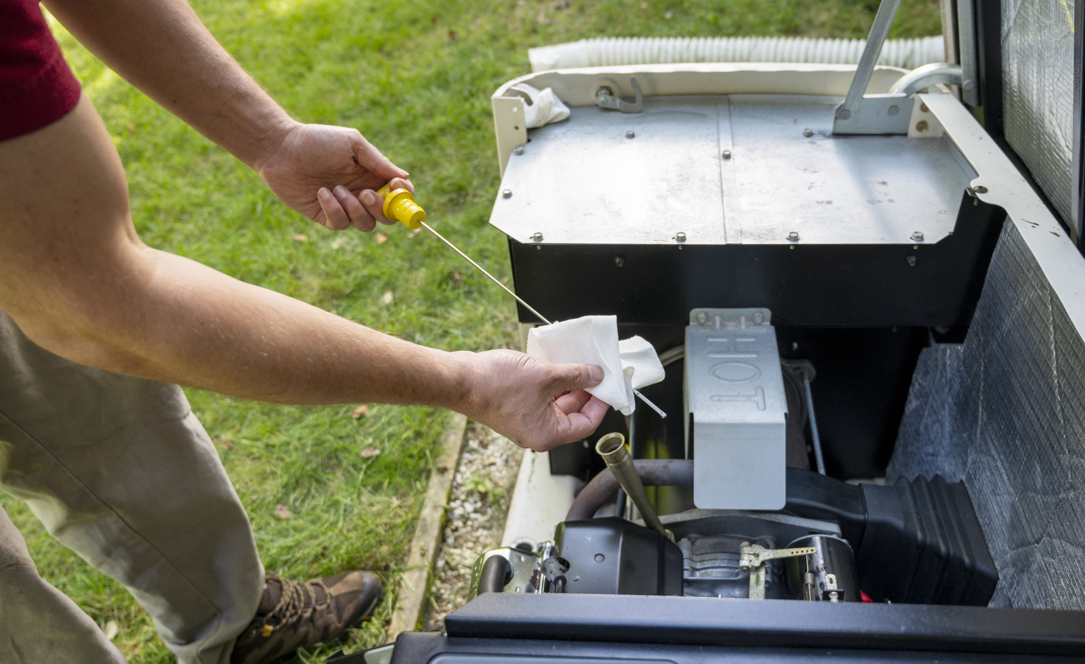 Man checking oil level on a home generator engine with a dipstick, wiping it clean with a paper towel outdoors.