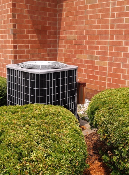 Outside residential heat pump unit by a red brick building. Transitioning your heat pump.